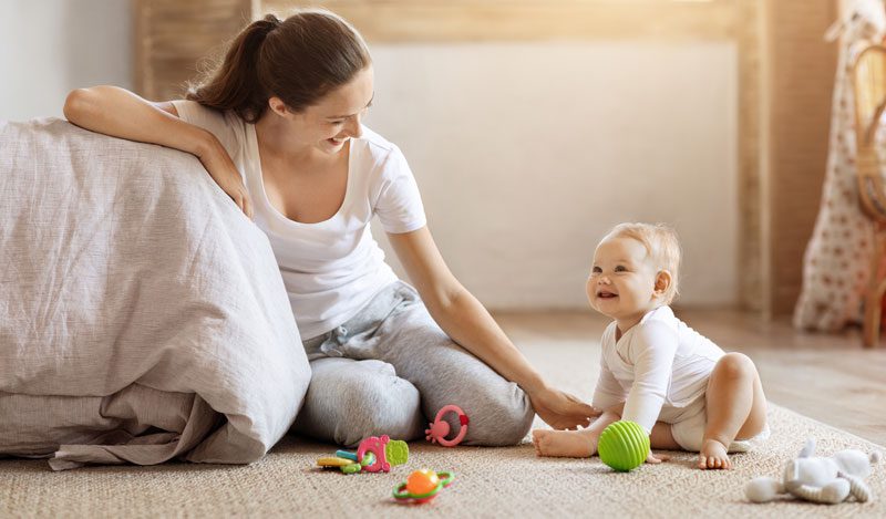 Mutter spielt mit ihrem Baby auf dem Teppich im Wohnzimmer